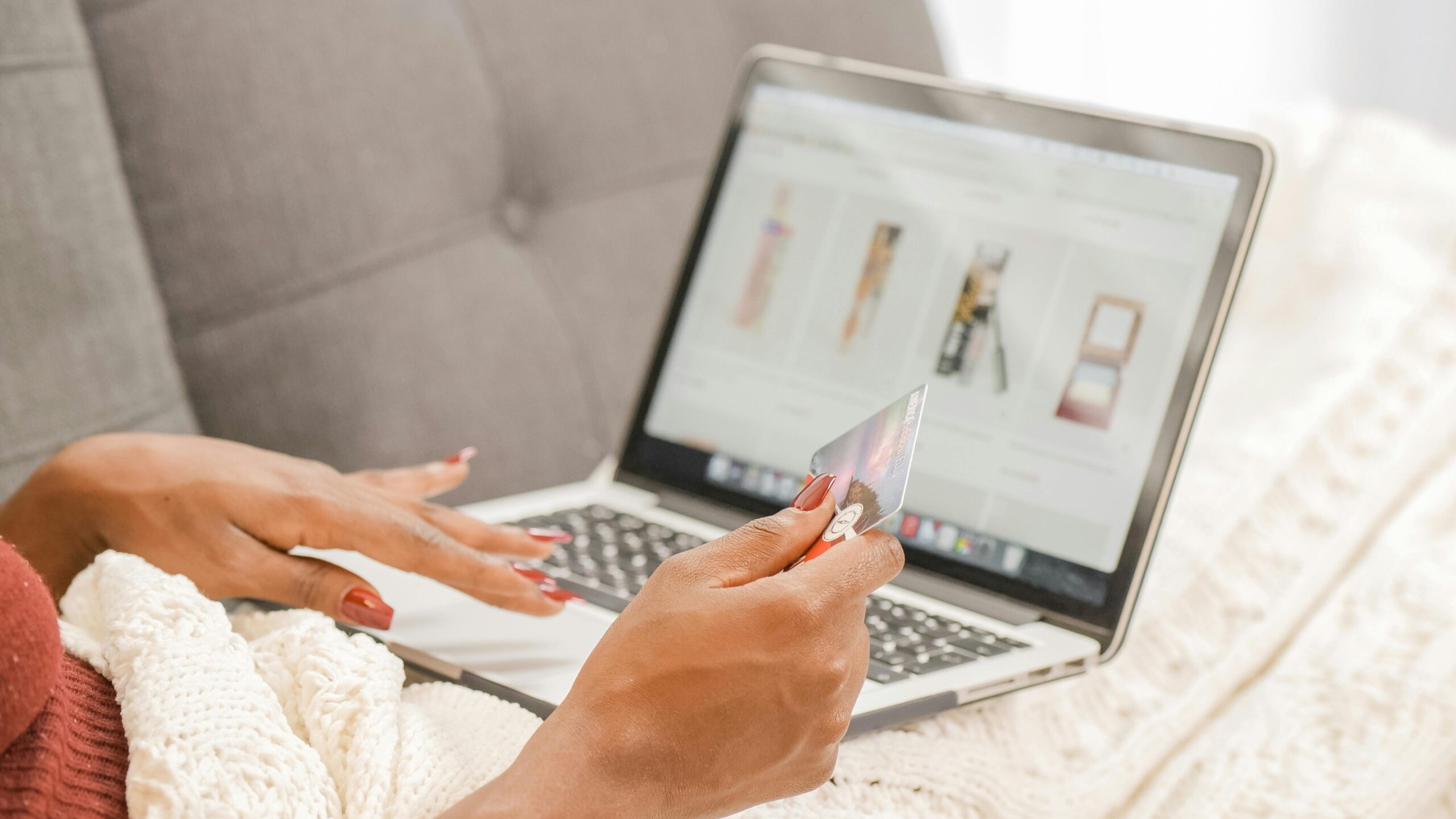 A woman relaxes on a couch while shopping online using her laptop and credit card.